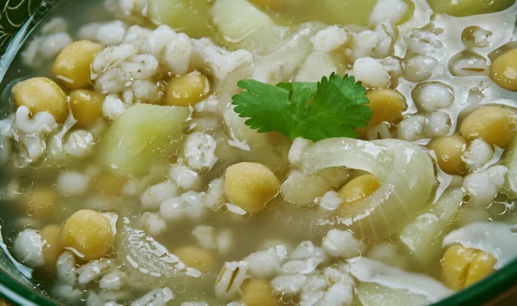 Gros plan sur la soupe Makhlouta mettant en valeur les pois chiches, l’orge et les courgettes dans un bouillon clair.