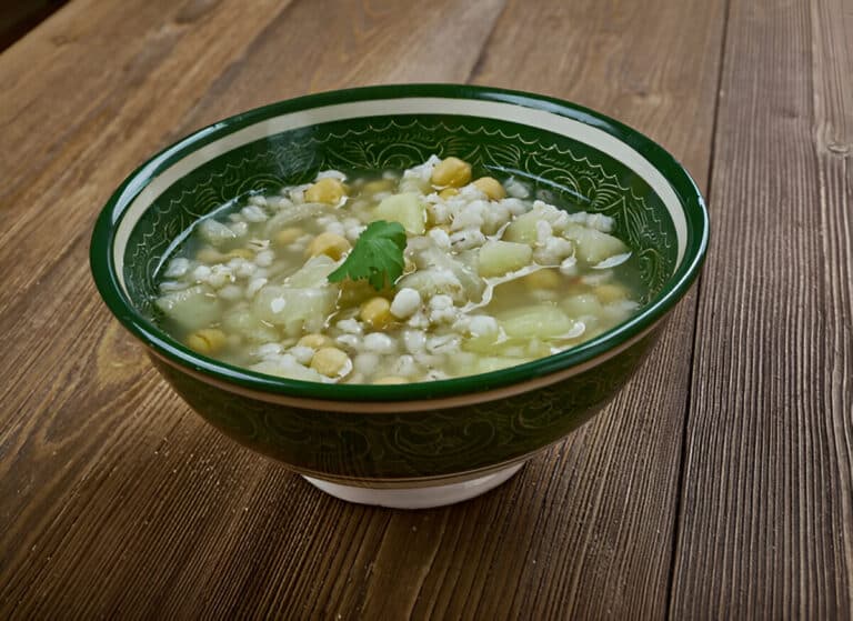 Bol de soupe Makhlouta fumante, vue en angle, sur une table rustique en bois.