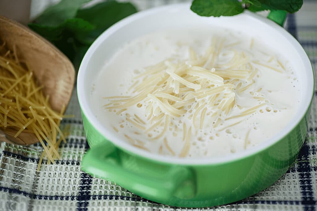 Bol de soupe au lait avec vermicelles fins dans une casserole verte, posée sur une nappe à carreaux.