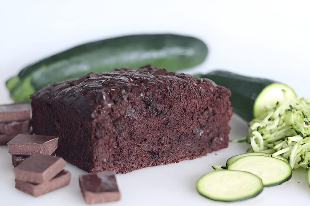Gâteau au chocolat avec courgette râpée et chocolat en morceaux devant, fond blanc épuré