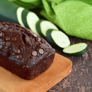 Tranche de gâteau chocolat courgette sur planche en bois avec rondelles de courgettes en arrière-plan
