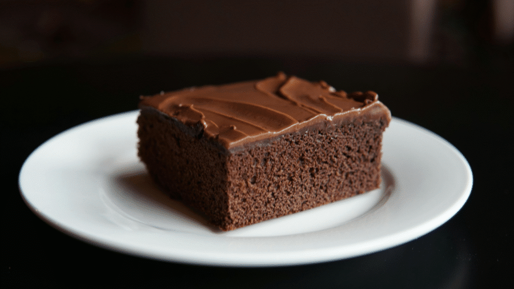 Carré de gâteau moelleux au chocolat avec glaçage brillant, servi sur une assiette blanche.