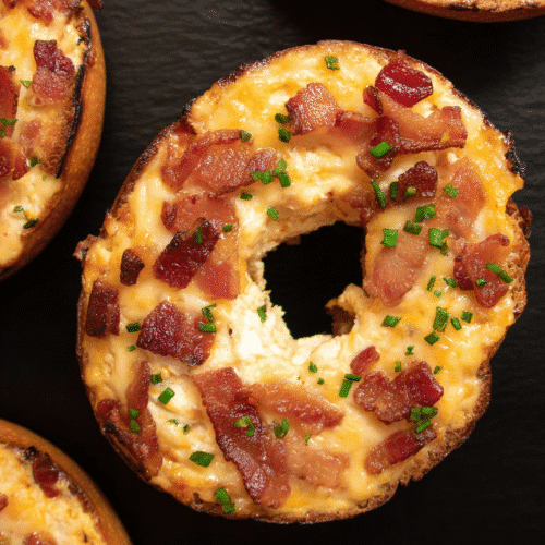 Toasted bagel topped with creamy cheese, crispy bacon, and chives on black background