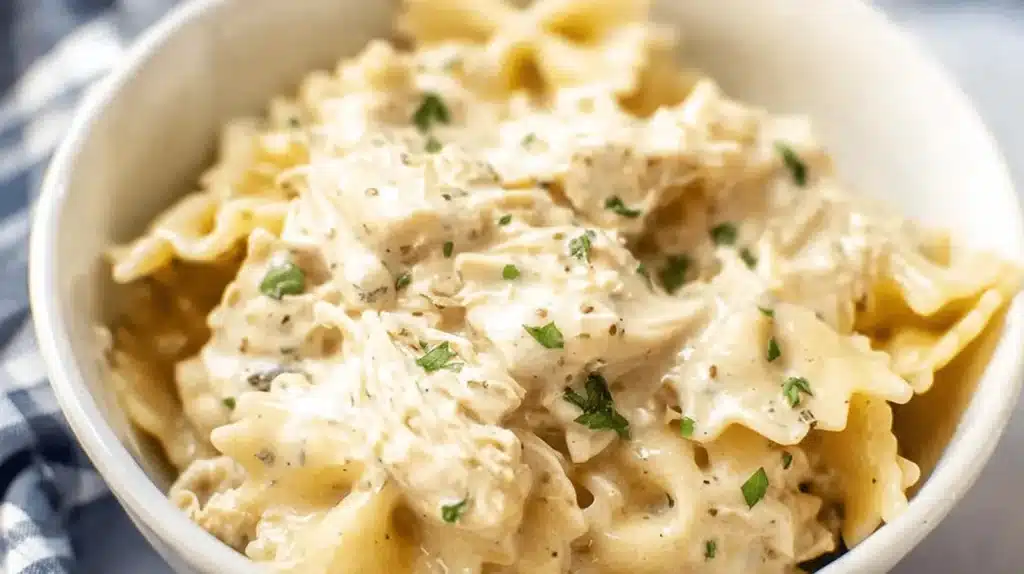 Appetizing close-up of creamy ranch chicken crockpot pasta with farfalle and shredded chicken, topped with fresh herbs.
