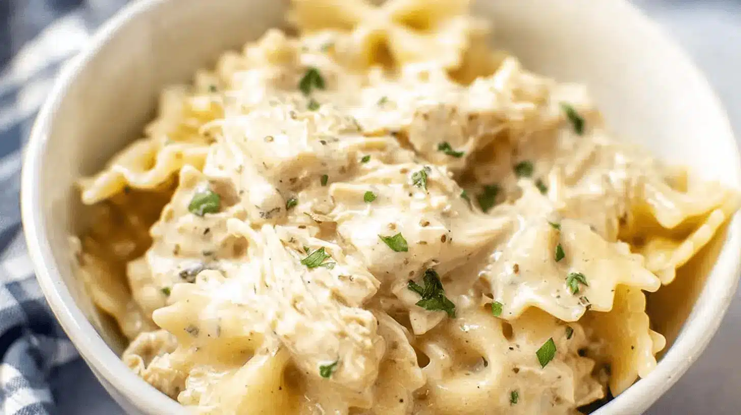 Appetizing close-up of creamy ranch chicken crockpot pasta with farfalle and shredded chicken, topped with fresh herbs.
