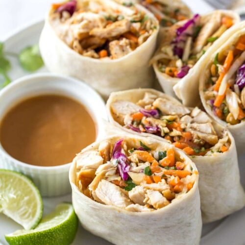 Close-up of Thai Peanut Chicken Wraps with vegetables and peanut sauce on a white plate