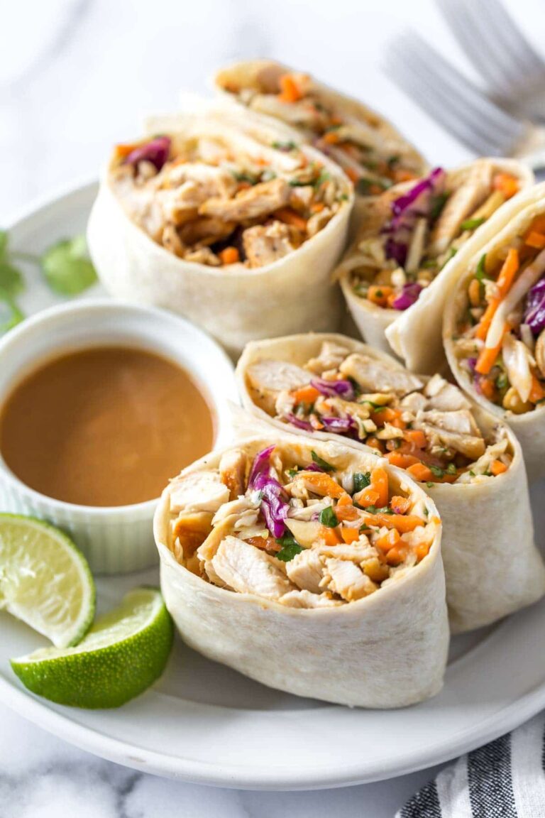 Close-up of Thai Peanut Chicken Wraps with vegetables and peanut sauce on a white plate
