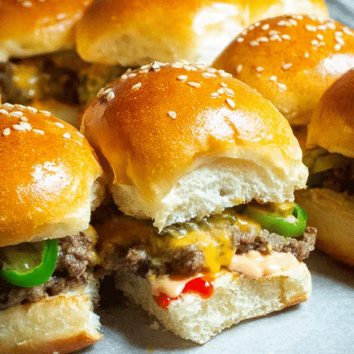Juicy mini cheeseburger slider with melted cheddar, pickles and sesame bun closeup.