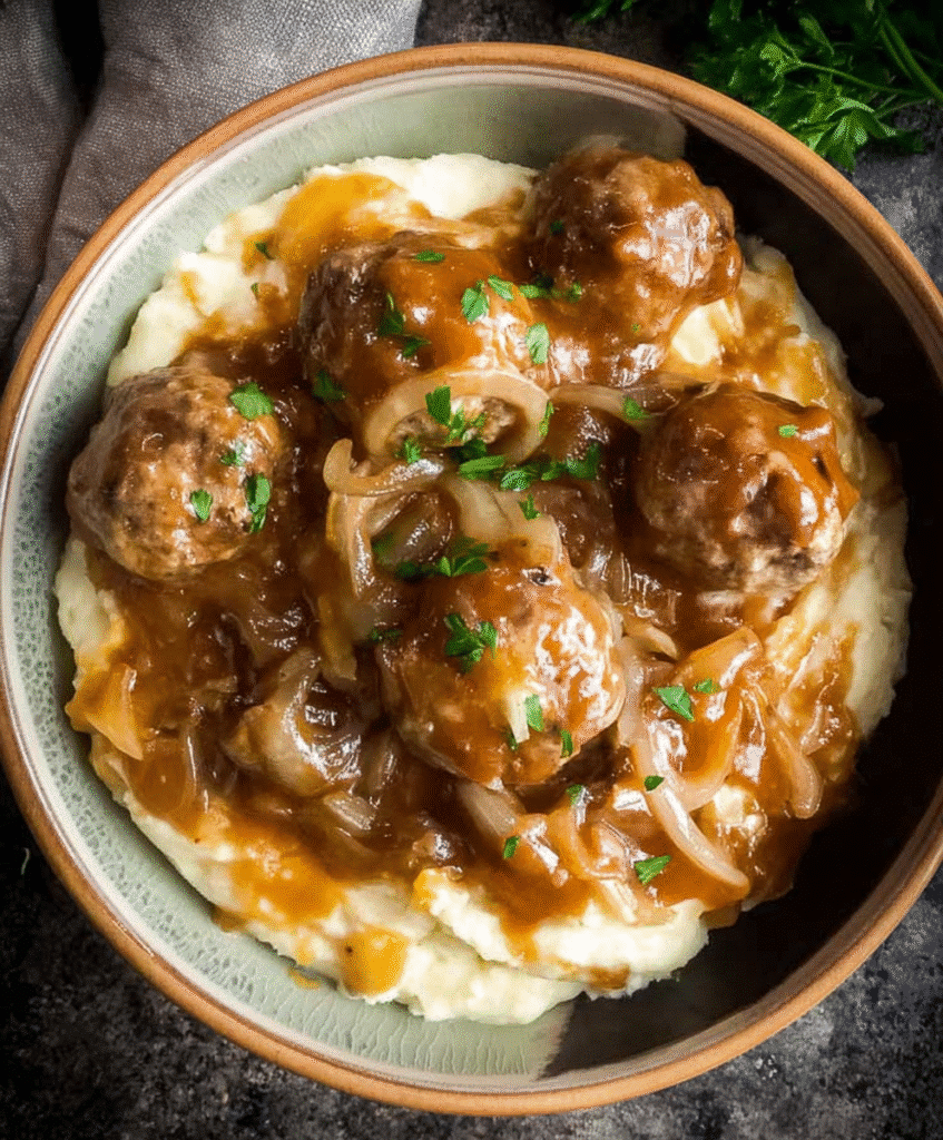 Close-up of Crockpot French Onion Meatballs served over creamy mashed potatoes, topped with caramelized onions and rich brown gravy, garnished with fresh parsley.