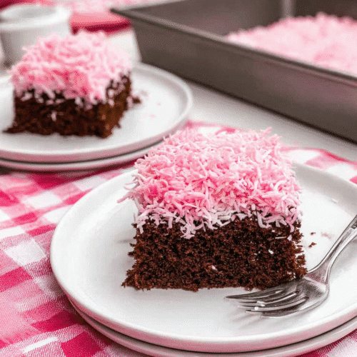 Slice of chocolate coconut cake topped with fluffy pink shredded coconut frosting on a white plate.