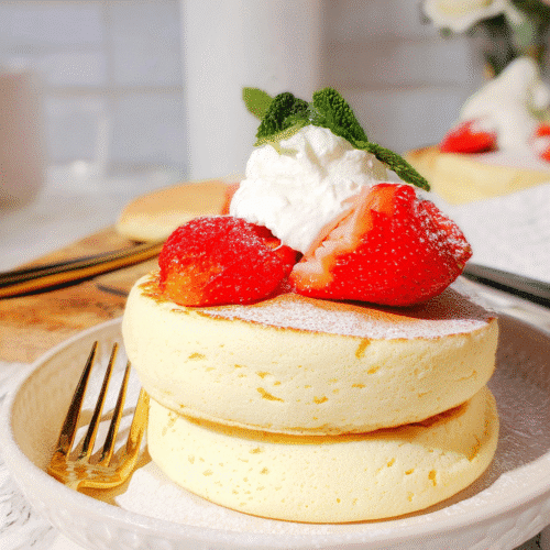 Fluffy Japanese souffle pancakes topped with whipped cream and fresh strawberries