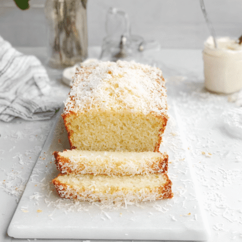 Homemade moist coconut loaf cake sliced on white marble board with shredded coconut