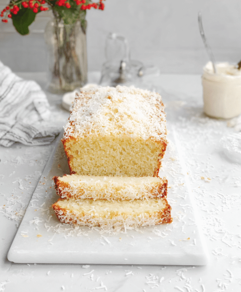Homemade moist coconut loaf cake sliced on white marble board with shredded coconut