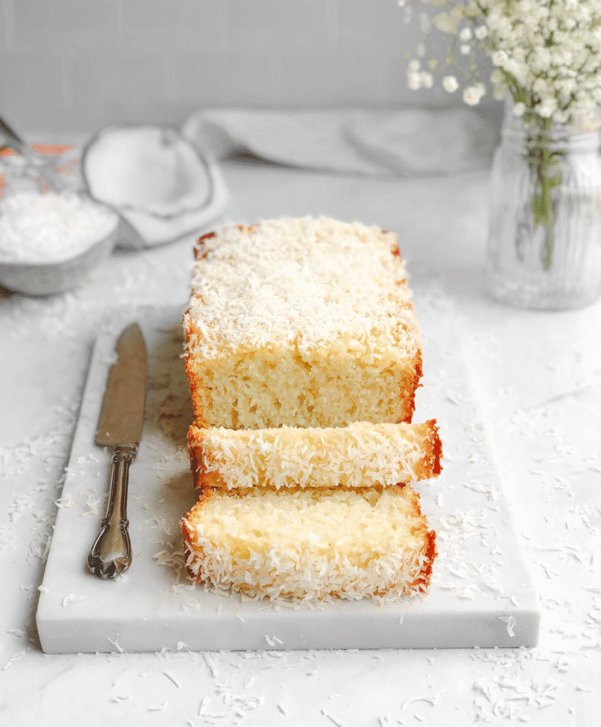 Soft and fluffy coconut bread with shredded coconut topping and knife on marble surface