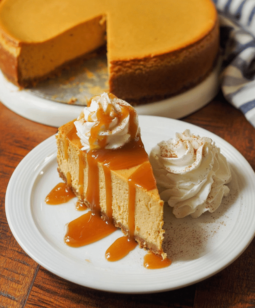Slice of pumpkin cheesecake drizzled with caramel and topped with whipped cream on a white plate.