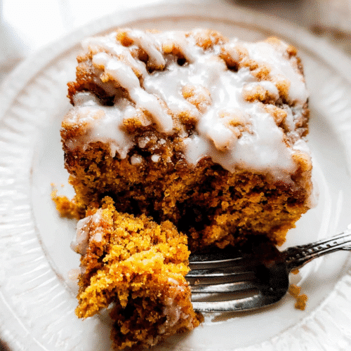 Pumpkin spice coffee cake with crumb topping and icing drizzle, served on a white plate with a fork.