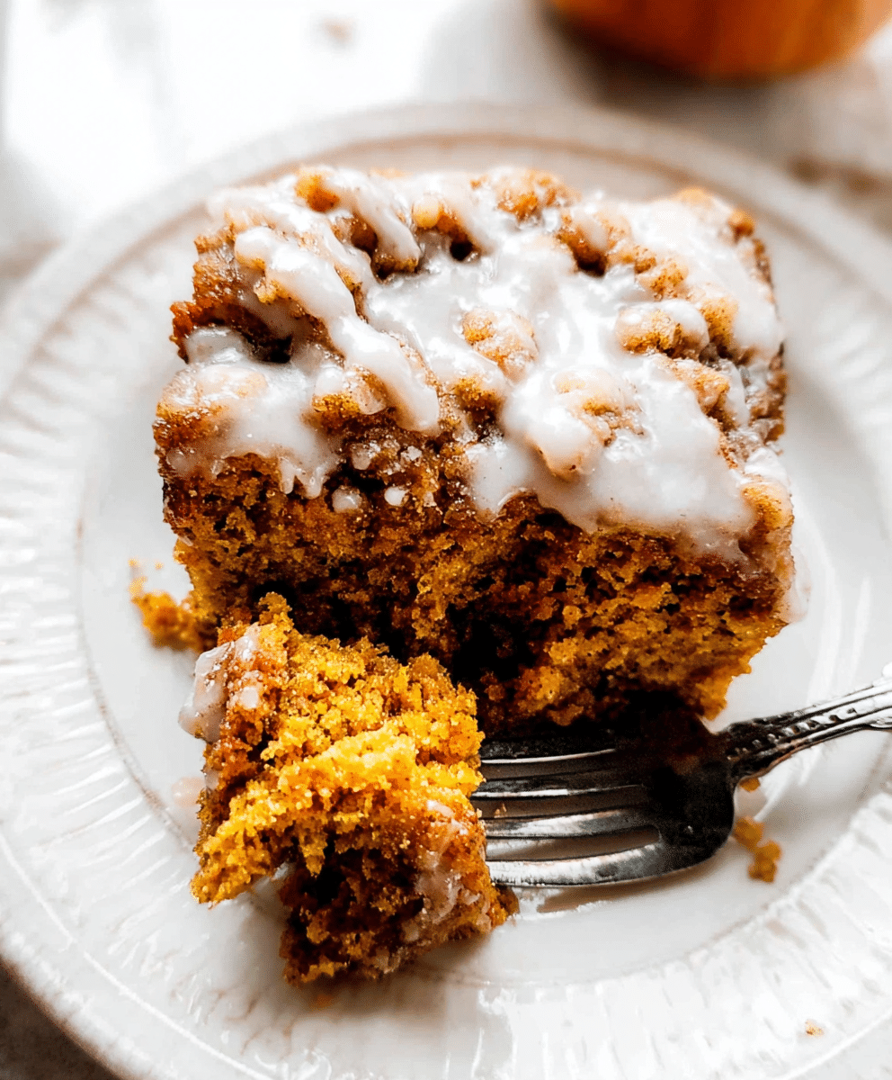 Pumpkin spice coffee cake with crumb topping and icing drizzle, served on a white plate with a fork.
