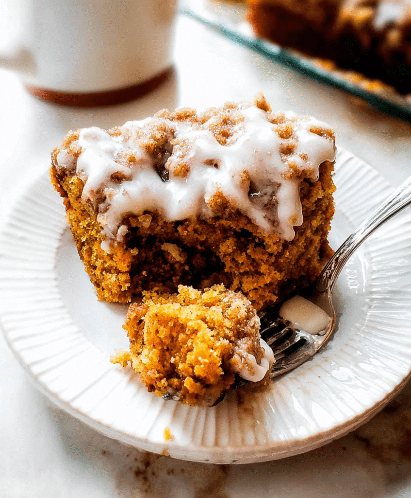 Close-up of a moist pumpkin coffee cake slice topped with cinnamon crumble and sweet vanilla glaze on a white plate.
