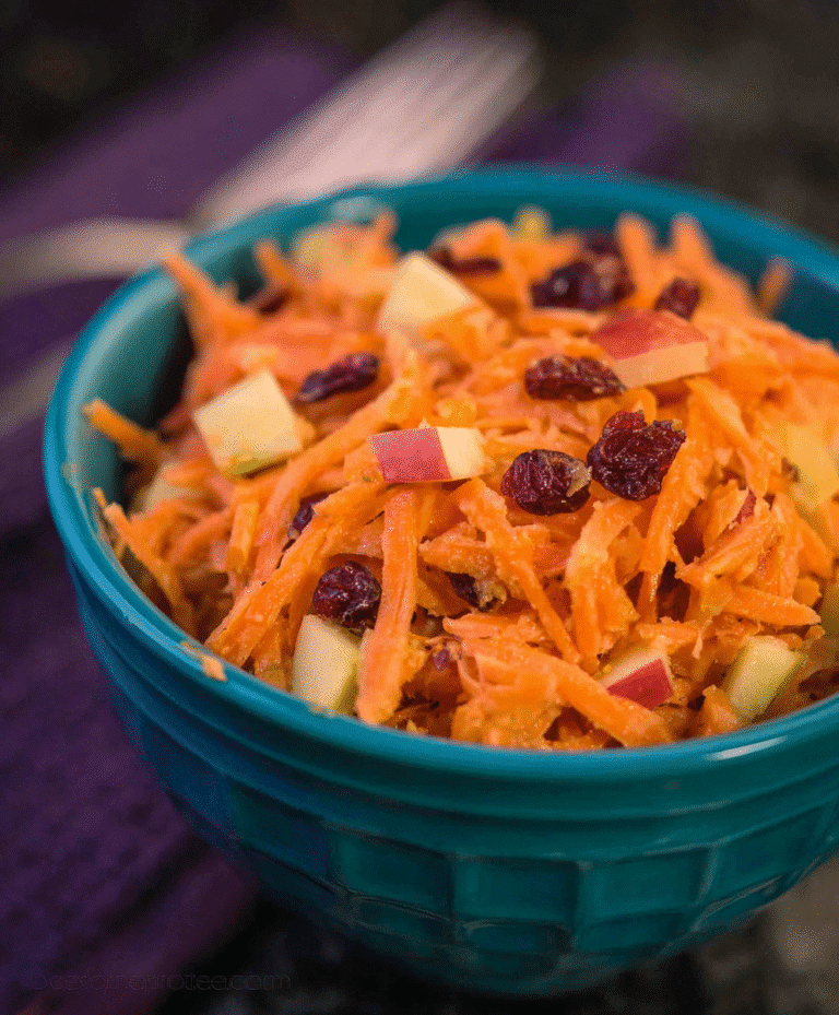 Fresh shredded carrot and apple salad mixed with dried cranberries in a teal bowl on dark background, healthy and vibrant.