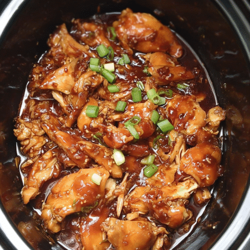 Tender chicken cooked in a sweet honey garlic sauce, topped with green onions and sesame seeds, in a slow cooker.