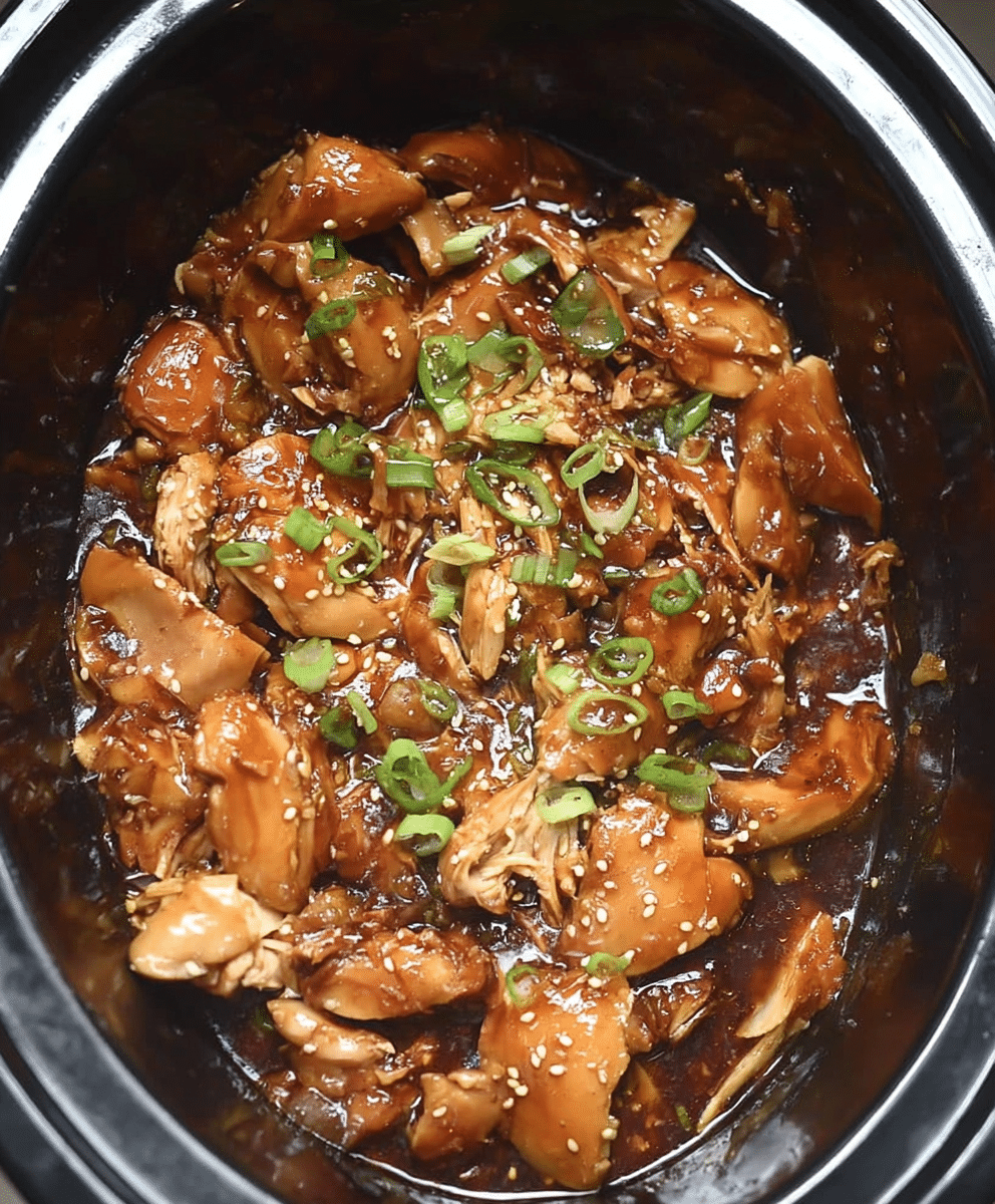 Tender chicken cooked in a sweet honey garlic sauce, topped with green onions and sesame seeds, in a slow cooker.