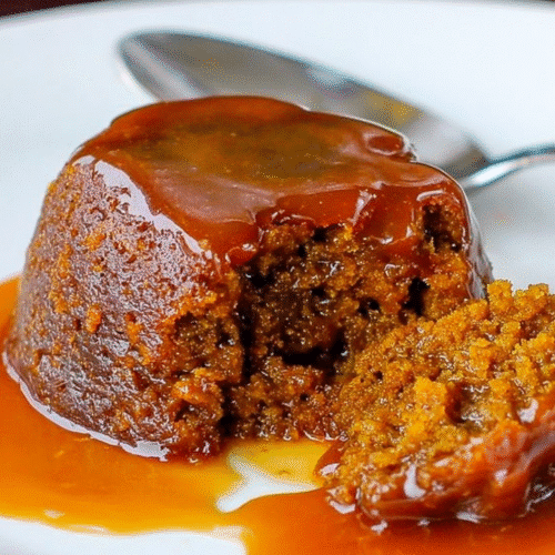 Warm sticky toffee pudding with rich caramel sauce, moist sponge cake broken open on a white plate.