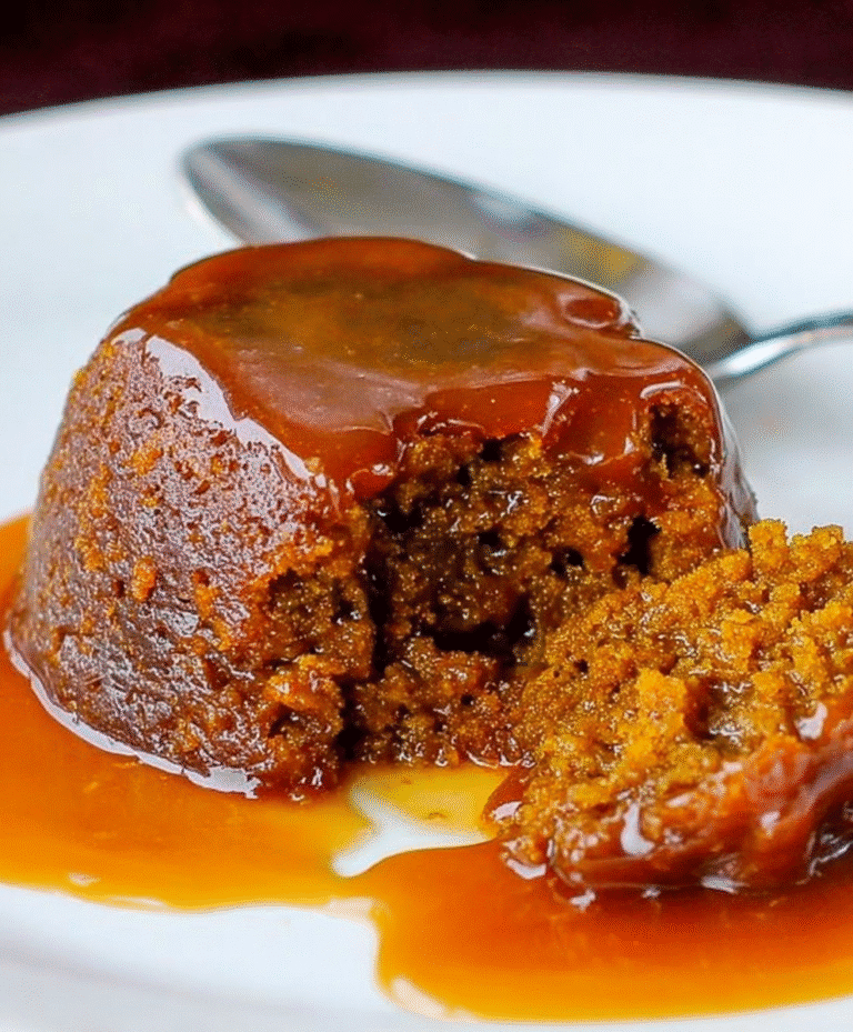 Warm sticky toffee pudding with rich caramel sauce, moist sponge cake broken open on a white plate.