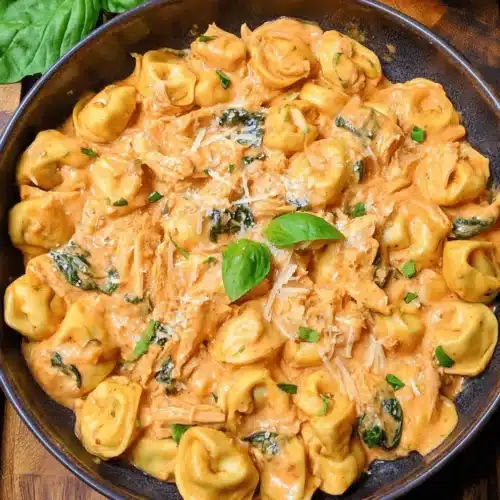 Close-up of creamy CrockPot Chicken Tortellini garnished with fresh basil and Parmesan cheese in a rustic bowl.