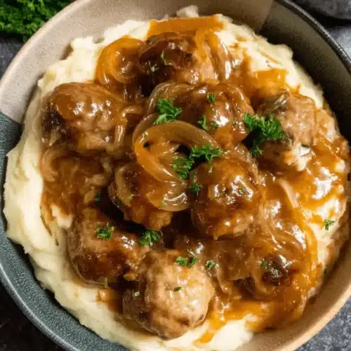 A close-up, top-down view of savory Crockpot French Onion Meatballs served over creamy mashed potatoes, garnished with fresh parsley.
