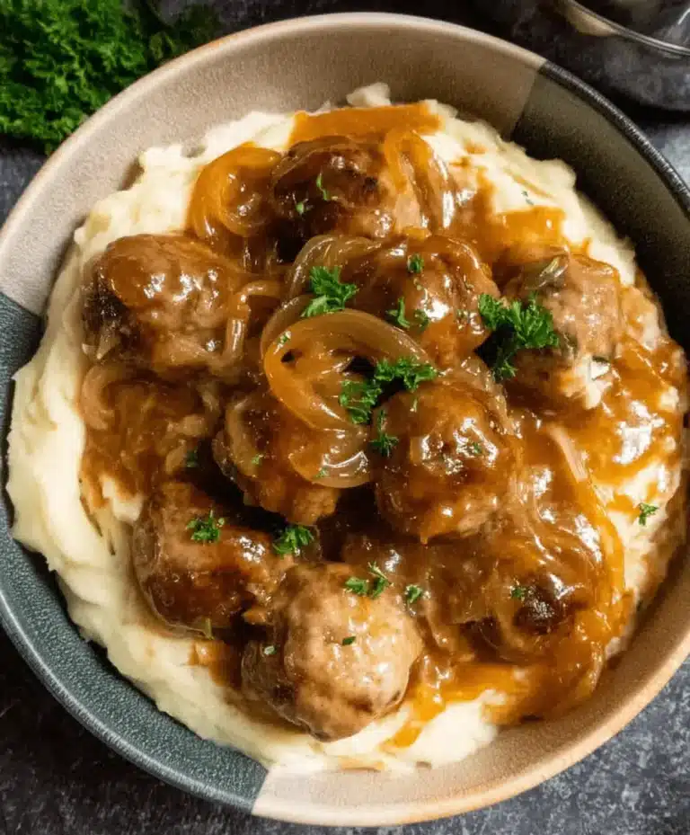 A close-up, top-down view of savory Crockpot French Onion Meatballs served over creamy mashed potatoes, garnished with fresh parsley.