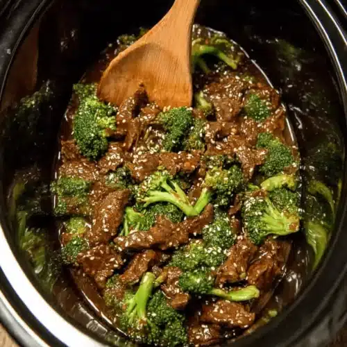 A top-down view of a Mouthwatering Crock Pot Beef And Broccoli dish simmering in a black slow cooker, garnished with sesame seeds.