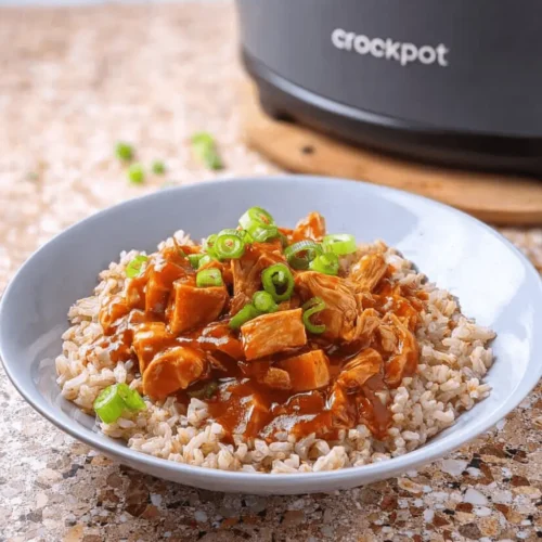 An appetizing bowl of Sweet Hawaiian Crock Pot Chicken with fluffy rice and green onions, with a Crock Pot in the blurred background.