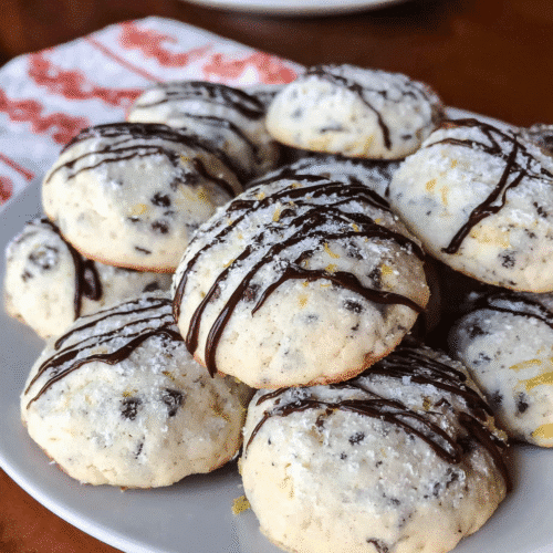 Soft cannoli cookies with chocolate chips, powdered sugar, and chocolate drizzle on white plate, Italian Christmas cookie recipe.
