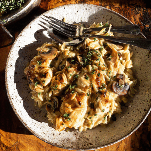 Creamy French onion chicken with mushrooms and orzo pasta, garnished with fresh parsley, served on rustic plate, cozy comfort food.