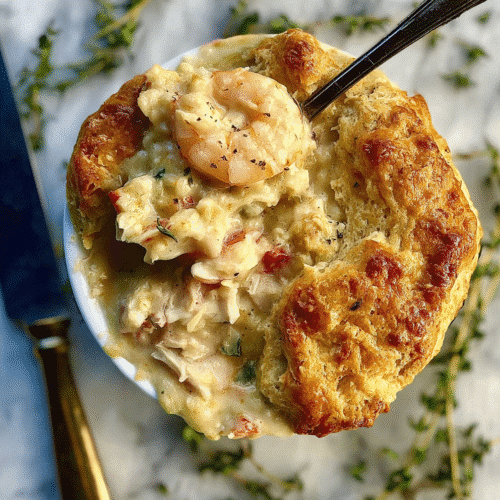 Golden flaky biscuit crust on a creamy lobster and shrimp pot pie, topped with fresh thyme, served in a white ramekin on a marble background.